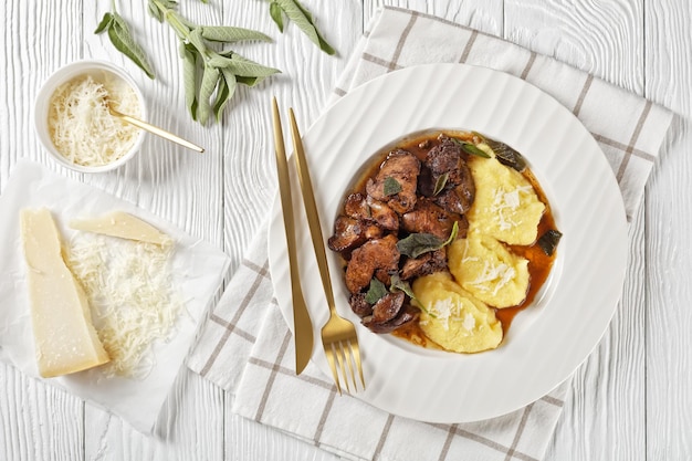 Fígado de frango com sálvia servido com polenta em um prato branco na mesa de madeira clara Fegatini di pollo alla salvia cozinha italiana