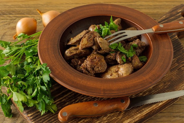 Fígado de frango cozido com cebola em um prato servido na mesa de madeira. Estilo rústico.