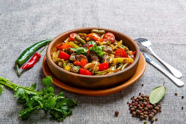 Fígado de frango estufado com legumes em um prato de barro. Pedaços de fígado, cebola, vagem, tomate.