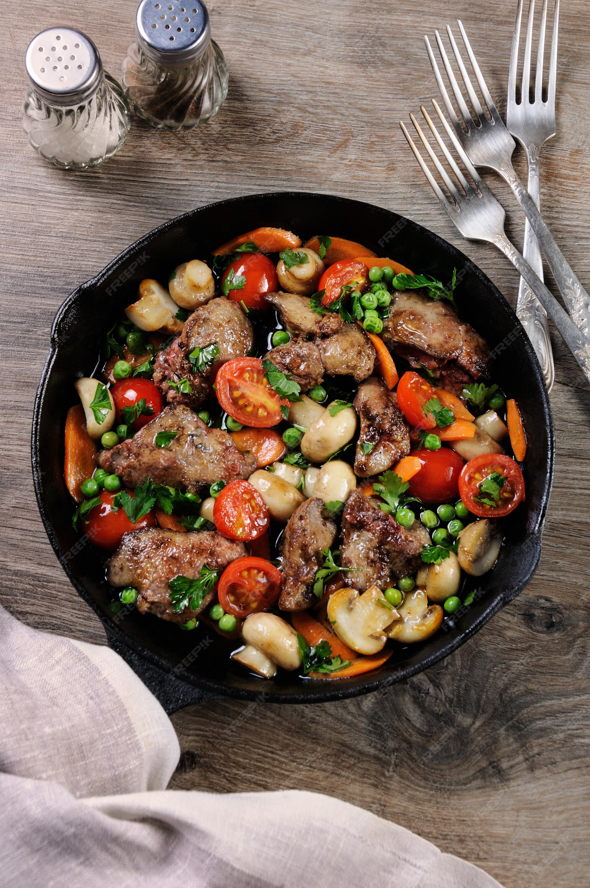 Fígado de frango frito com acompanhamento de vegetais de tomates, cenouras,  cogumelos e ervilhas em uma panela