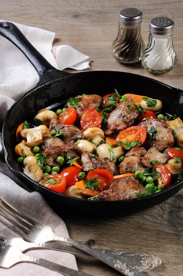 Fígado de frango frito com acompanhamento de vegetais de tomates, cenouras,  cogumelos e ervilhas em uma panela