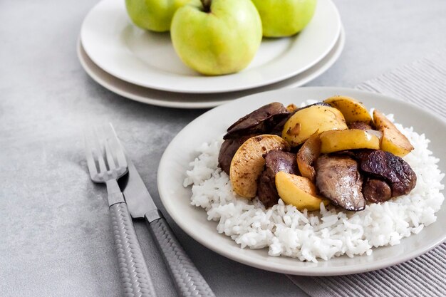 Fígado de frango frito com maçãs servido com arroz branco em um prato. maçãs verdes na superfície