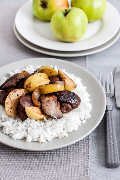 Fígado de frango frito com maçãs servido com arroz branco em um prato.