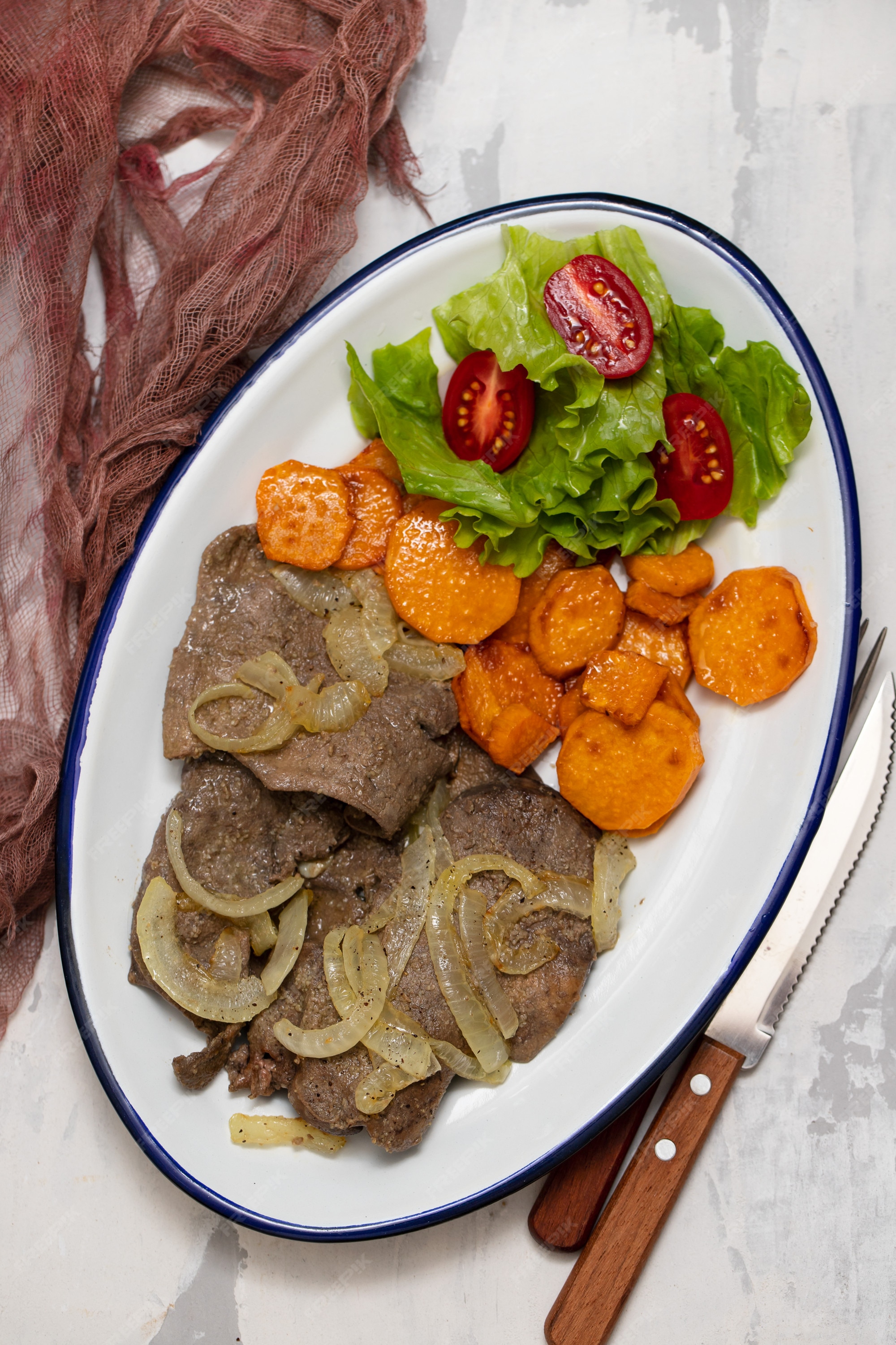 Fígado frito com cebola, batata doce e salada no prato branco