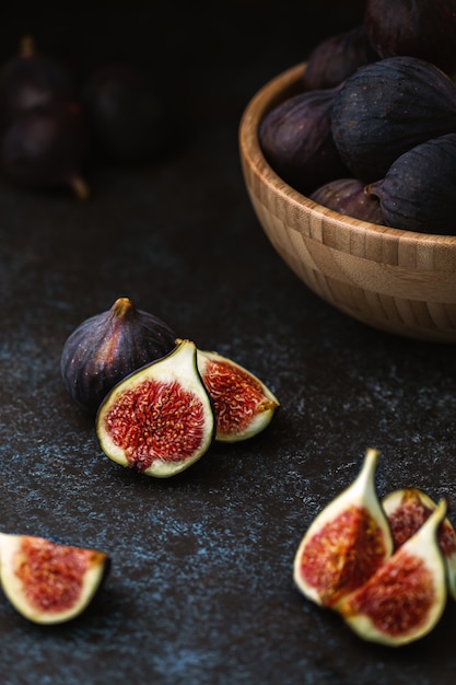 Foto figos fatiados na mesa e frutas maduras em uma tigela de madeira