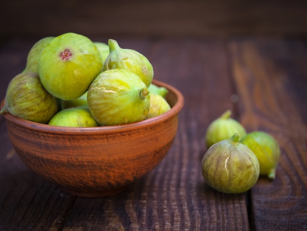 Figos maduros verde-amarelos em uma xícara de barro em uma mesa de madeira