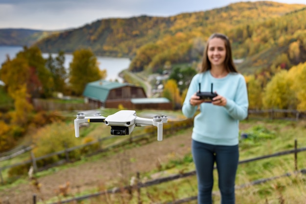 Figura borrada de menina controla um drone no outono fundo desfocado. Conceito de foco suave com montanha e lago