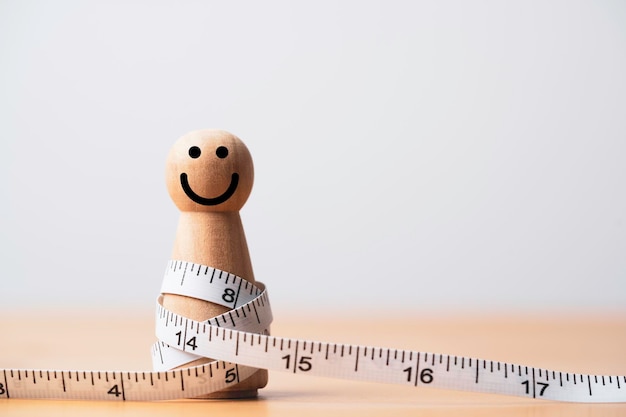 Figura de madeira gorda com fita métrica para dieta feliz e conceito de perda de peso