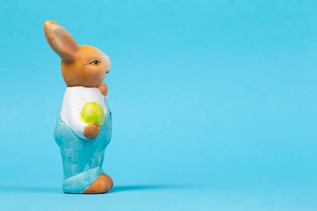 Figura de um coelhinho da Páscoa de pelúcia com um ovo em um cartão de Páscoa de fundo azul
