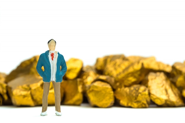 Figura empresário em miniatura com pilha de pepitas de ouro