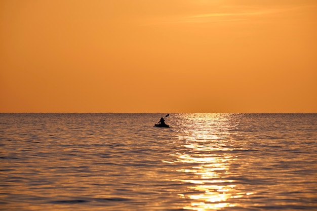 Figura escura de esportista remando sozinho em seu barco de caiaque na água do mar ao pôr do sol Conceito de esportes radicais ativos