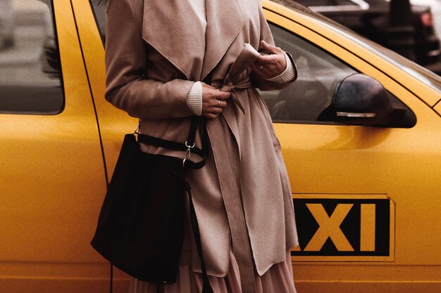 Figura femenina en el abrigo largo marrón contra el taxi amarillo Concepto de estilo callejero de ropa de otoño