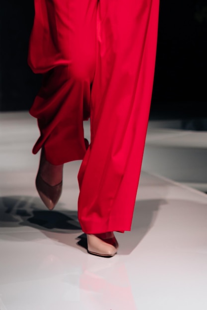 Figura femenina recortada vestida con pantalones rojos clásicos y tacones altos caminando por la pasarela