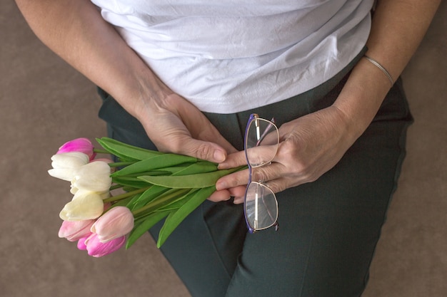 La figura femenina sin rostro tiene en las manos un ramo de tulipanes blancos y rosas y gafas. Día de la Madre