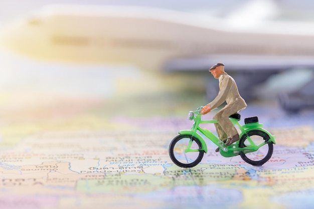 Figura hombre de negocios en bicicleta en el mapa mundial con fondo de avión blanco borroso