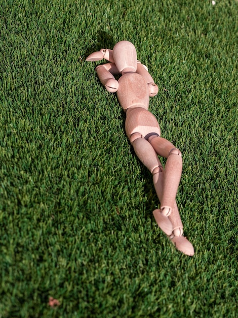 Figura humana de madera tirada en la hierba tomando el sol