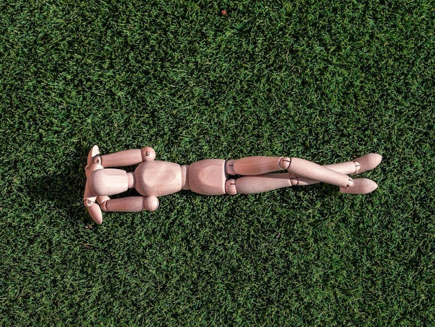 Figura humana de madera tirada en la hierba tomando el sol