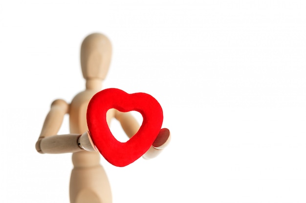 La figura de madera de un hombre sostiene en sus manos un corazón rojo sobre una superficie blanca, le da el corazón