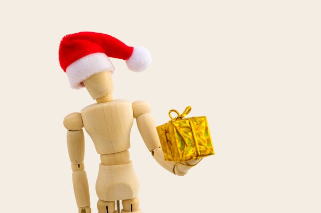 Figura de madera - maniquí de arte con gorro de Papá Noel rojo con caja de regalo. Concepto de negocio y diseño para Navidad. Enfoque selectivo