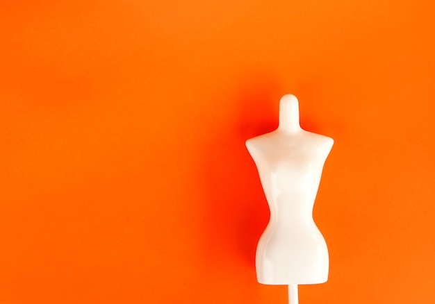 Foto figura de maniquí femenino de plástico blanco sobre fondo naranja brillante.