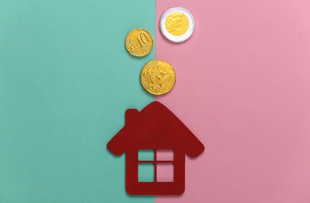 Foto figura mini casa con monedas sobre un pastel azul-rosa. presupuesto familiar