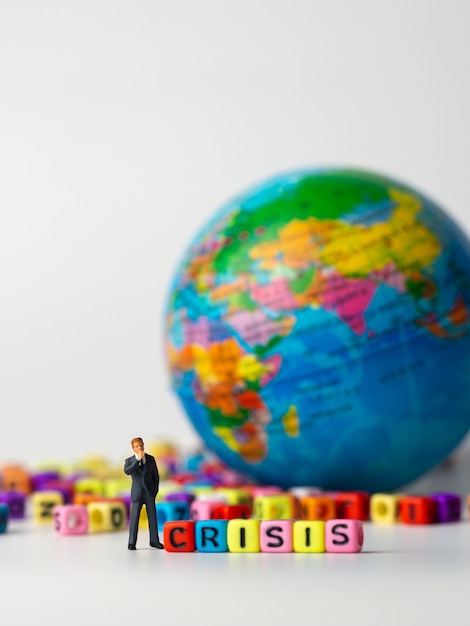 Foto figura miniatura de hombre de negocios que se encuentra en la parte trasera del colorido alfabeto de crisis y el globo en el fondo