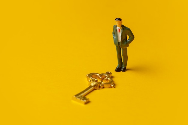 Foto figura en miniatura de un hombre pulcra llave de oro sobre fondo amarillo