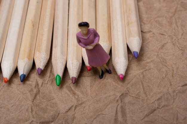 Figura de mujer junto a un manojo de lápiz con cuerpo de madera y puntas de colores