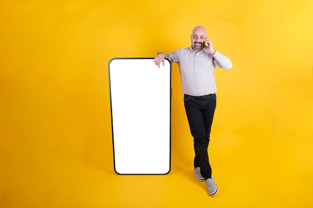 Figura paterna homem milenar falando ao telefone e inclinando-se grande smartphone com tela branca em branco