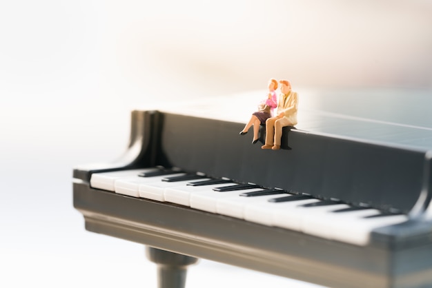 Foto figura pequena dos pares que senta-se no mini piano.