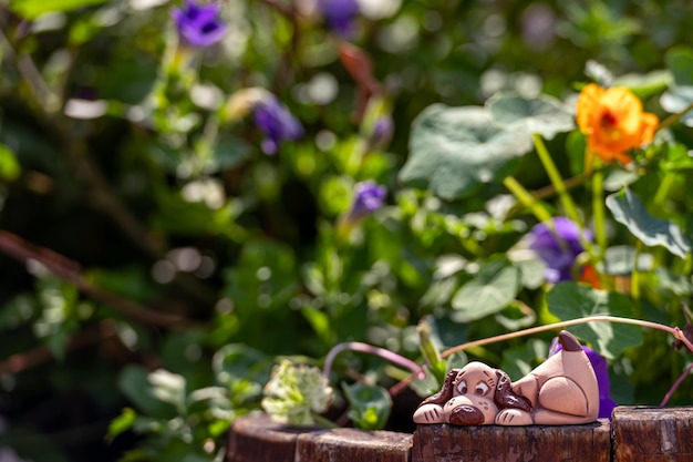 Figura de perro de arcilla en el jardín entre plantas y flores en primer plano