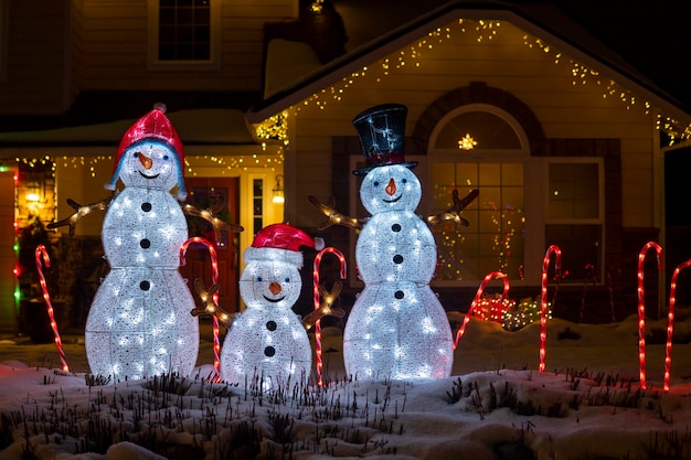 Figuras brilhantes de bonecos de neve à noite. Lindas decorações iluminadas de Natal fora de casa