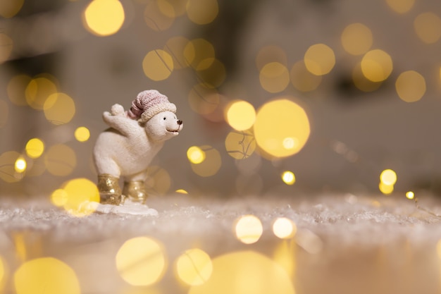 Figuras decorativas de temática navideña. La estatuilla de un cachorro de oso blanco tiene una bola de nieve detrás. Decoración del árbol de navidad. Decoración festiva, cálidas luces bokeh.