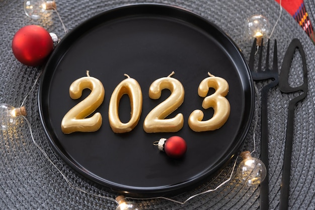 Figuras doradas 2023 de velas en un plato negro en una mesa festiva con un banquete de fiesta interior Loftstyle de servicio de Año Nuevo Cuchillo de tenedor de servilleta de mimbre