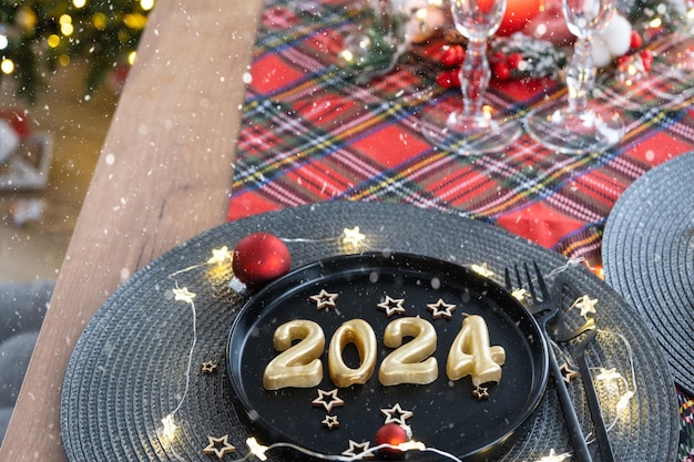 Figuras doradas 2024 de velas en un plato negro en una mesa festiva con un banquete de fiesta interior estilo Loft de Año Nuevo Servilleta de mimbre tenedor cuchillo