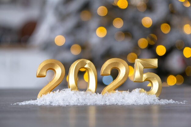 Figuras doradas número 2025 Año Nuevo contra el fondo de una pequeña casa con luz cálida y guirnaldas Tarjeta de felicitación Feliz Año Nuevo en una casa acogedora
