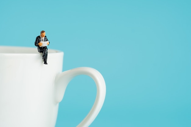 Foto figuras em miniatura de negócios sentado e ler um livro, ler jornal, esperando, conversando e relaxar na xícara branca de café quente.