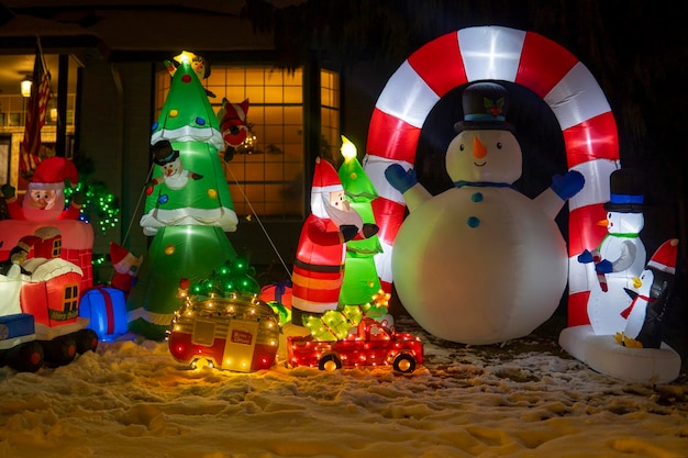 Figuras infláveis de boneco de neve, Papai Noel, trem e árvore de Natal brilhando à noite. Natal