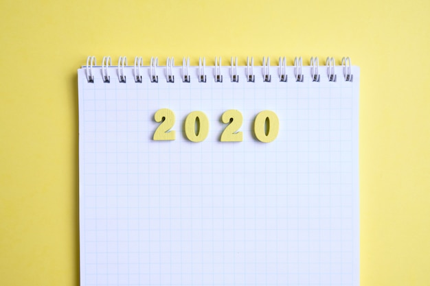 Figuras de madera 2020 al lado del cuaderno sobre un fondo amarillo. Vista superior.
