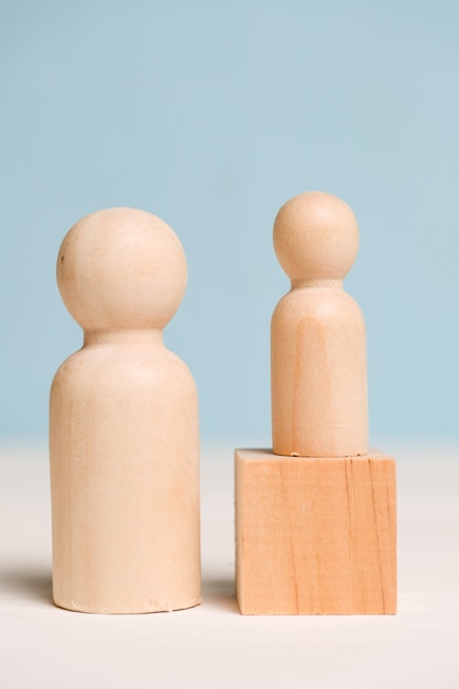 Figuras de madera con un cubo sobre un fondo azul. Concepto de tutoría. Un profesional enseña a un estudiante. De cerca.