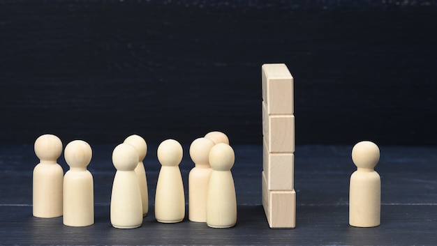 Figuras de madera de hombres, la multitud se para frente a una pared de bloques de madera, al otro lado una figura. El concepto de disputa y malentendido, una gran diferencia en las personas.