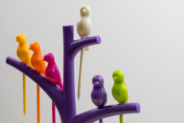 Figuras de pájaros de plástico multicolor sentados en un árbol sobre un fondo claro