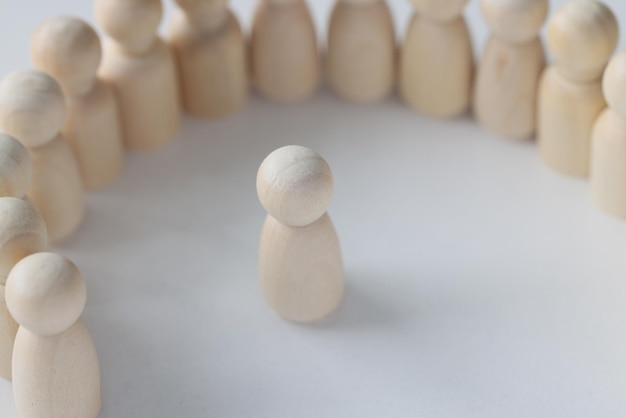 Figuras de personas de madera se paran en la superficie blanca lisa del concepto de mesa de intimidación y multitud
