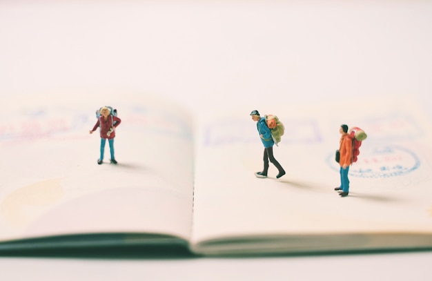 Figuras de personas en miniatura con mochila caminando y de pie en la página del pasaporte con sellos de inmigración, viajes y concepto de vacaciones