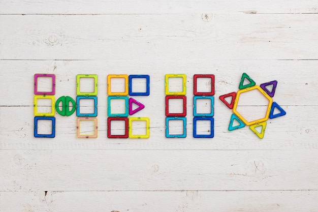 Figuras de plástico de colores yacen sobre una mesa de madera blanca Las piezas de plástico multicolores se presentan en la palabra HOLA Concepto de educación