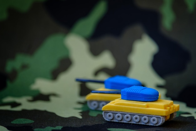 Foto figuras de tanques yello y azules sobre fondo de camuflaje colores de la bandera ucraniana en figuras de tanques de juguete concepto antibélico enfoque selectivo