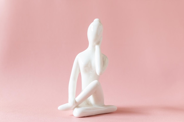 Figurilla de yoga de cerámica de mujer haciendo pose de yoga sobre fondo rosa