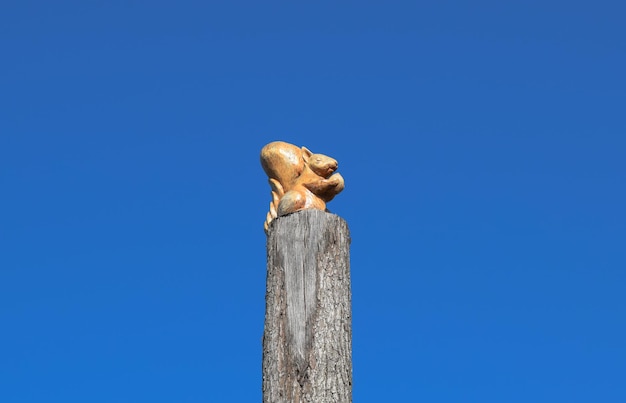 Figurina de ardilla con una nuez de un árbol en un tronco de árbol sobre un fondo de cielo azul Figuras de animales hechas de madera tallado en madera