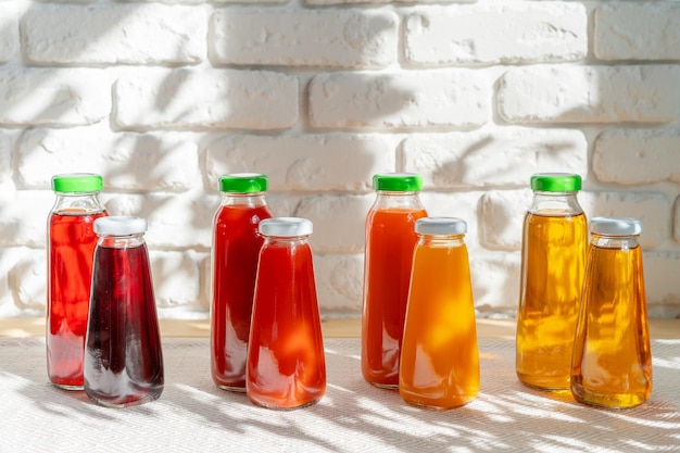 Foto fila de botellas de vidrio de diferentes jugos contra la pared de ladrillo blanco