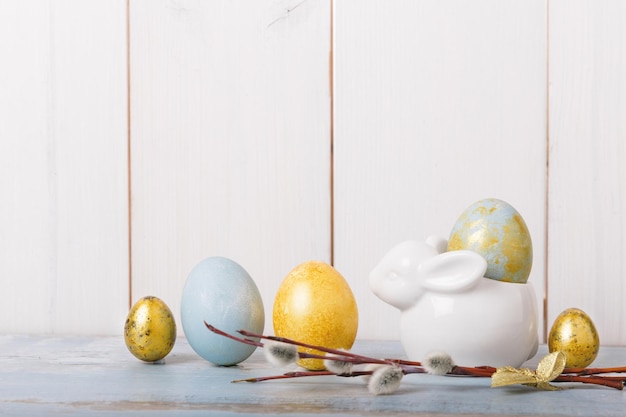 Fila de coloridos huevos de pascua azules y dorados conejito de pascua frente a una pared de madera blanca con espacio para texto Fondo de Pascua